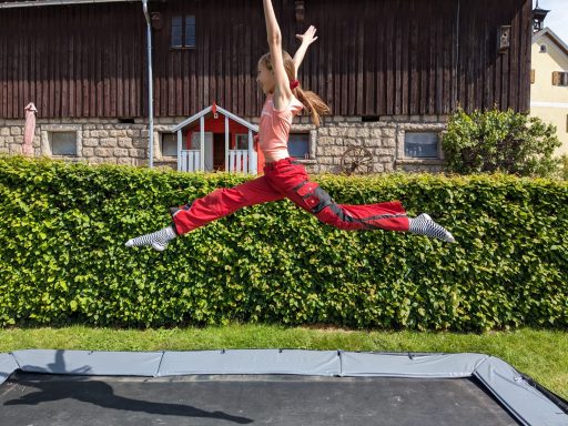 Ein Mädchen springt mit weit gespreizten Beinen auf einem Trampolin in der Luft.