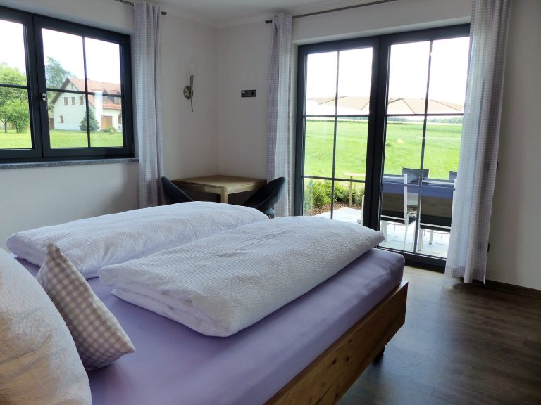 Helles Schlafzimmer mit Doppelbett und Blick auf die grüne Landschaft durch große Fenster.