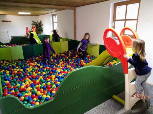 Kinder spielen in einem bunten Bällebad mit Rutschen und Spielgeräten.