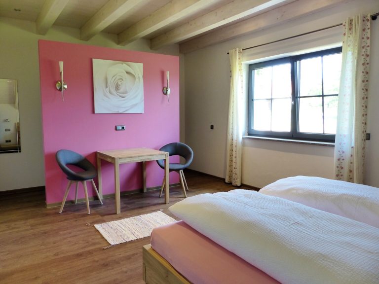 Helles Zimmer mit pinker Wand, zwei Betten und einem Tisch mit Stühlen.