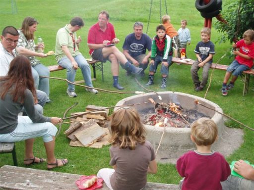 Gruppe von Menschen am Lagerfeuer, einige rösten Marshmallows und genießen die Zeit.