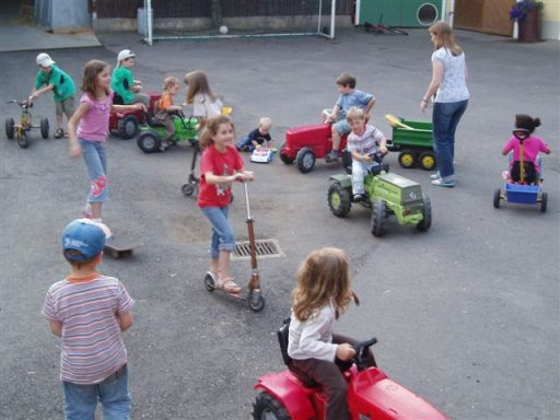 Kinder fahren auf Spielzeugautos und Roller auf einem Hof.