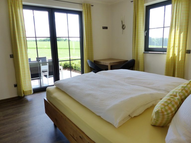 Helles Schlafzimmer mit großen Fenstern, Doppelbett und Blick auf die grüne Landschaft.