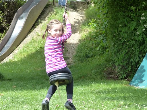 Mädchen schwingt fröhlich auf einer Reifen-Schaukel im Park.