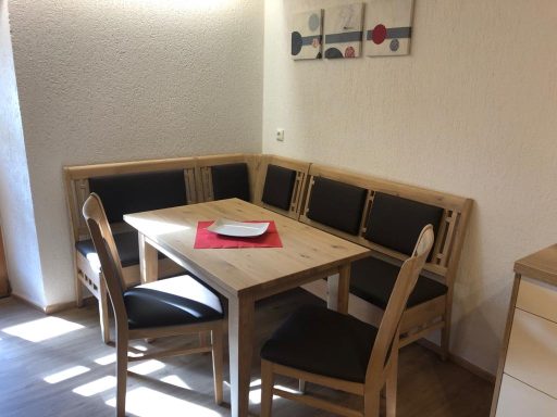 Holztisch mit Stühlen und einer gemütlichen Eckbank in einem hellen Raum.