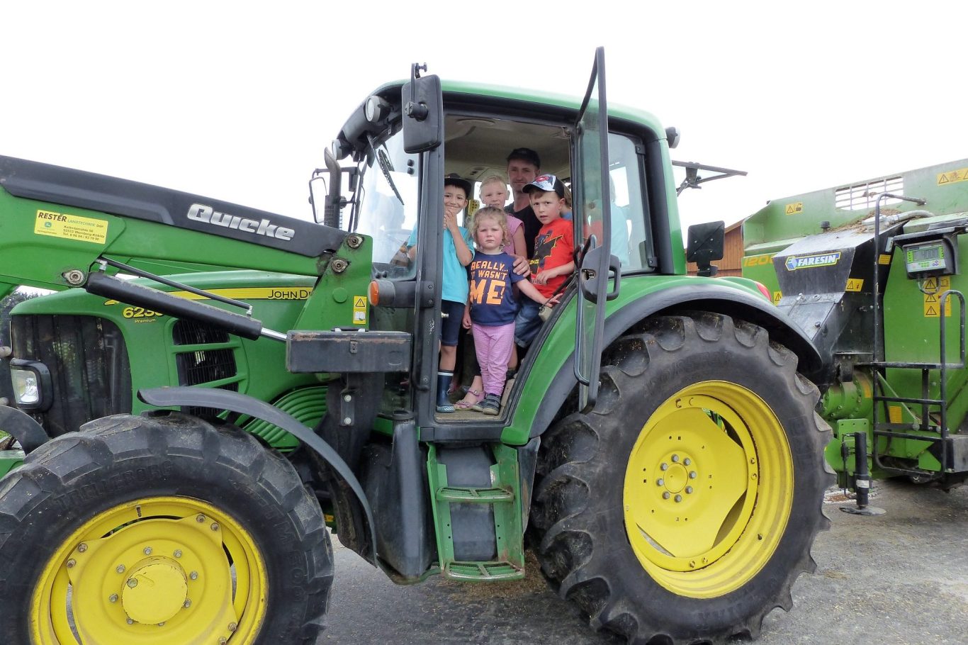 Kinder stehen fröhlich auf einem Traktor, umgeben von landwirtschaftlicher Ausrüstung.