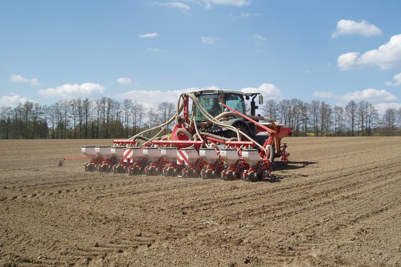 Traktor mit Pflug bearbeitet ein Feld unter blauem Himmel und wenigen Wolken.