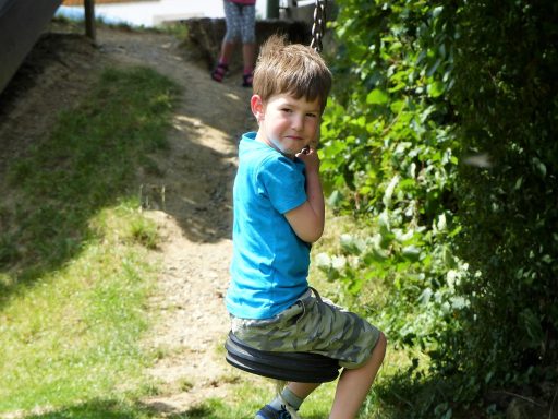 Junge in blauer T-Shirt sitzt auf einem Reifen im Freien, umgeben von Grün.