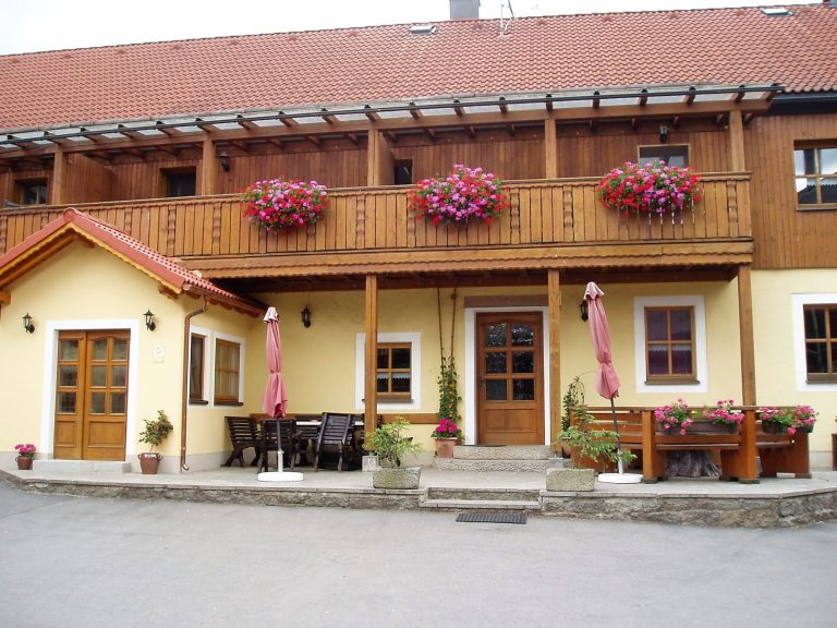 Hölzerne Fassade mit Balkon, blühenden Pflanzen und Sitzbereich im Freien.