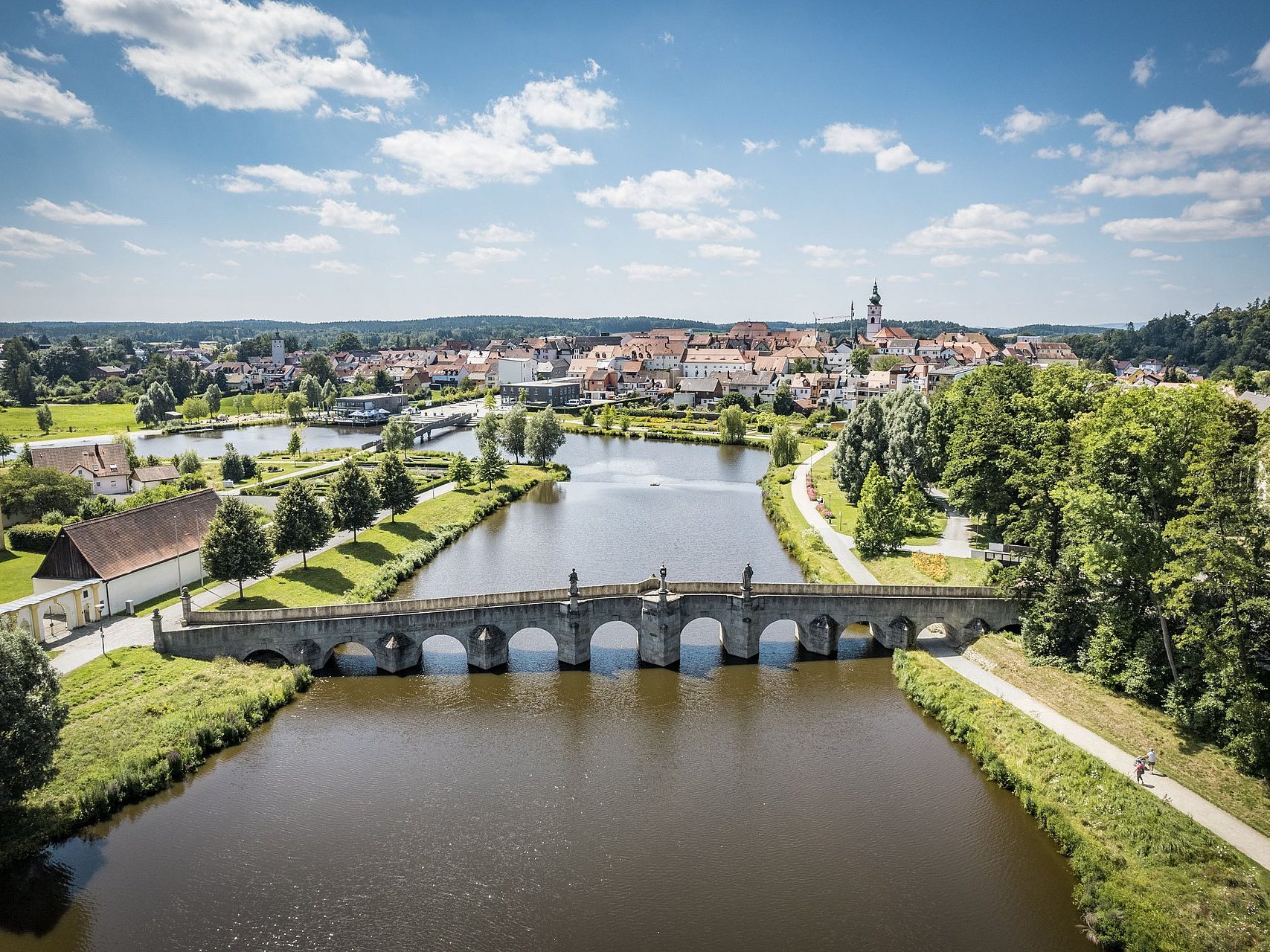 Blick auf eine Brücke über einen Fluss, umgeben von Bäumen und einer Stadtlandschaft.