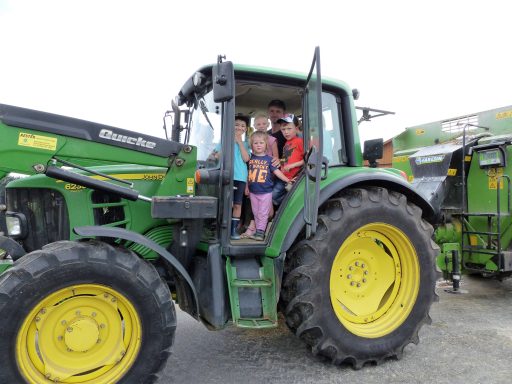 Kinder stehen auf einem Traktor und lächeln in die Kamera.