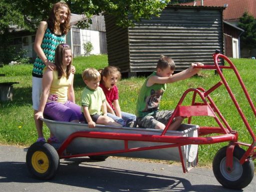 Fünf Kinder sitzen in einem offenen Wagen und lachen, während ein Junge ihn schiebt.